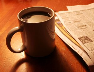 Ceramic coffee mug and newspaper on wood table.
